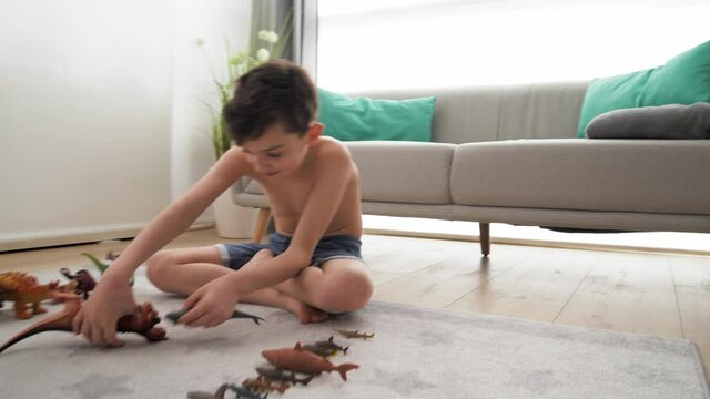 Dinosaur threatening boy playing with toys, sitting on carpet at home