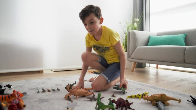 Boy sitting on carpet at home, play fighting with animal figurines