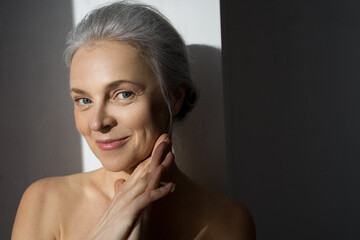 Aged woman with healthy glowing skin and toothy smile touching face gently