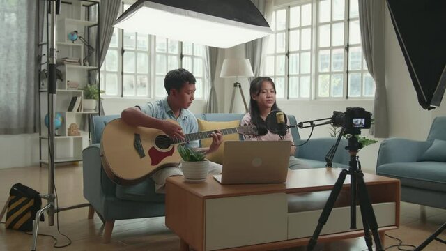 Asian Children Playing Guitar And Sing A Song While Streaming For Youtube Channel. The Children Is Broadcasting Live On The Internet. Professional Light Equipment
