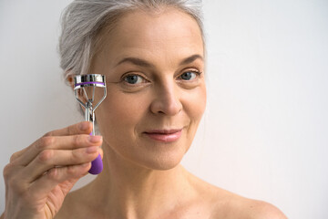 Woman looking at the camera with light smile and showing to the camera eyelash curlers