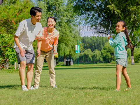 Happy family of three playing tennis in the park