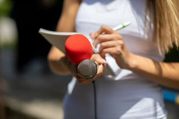 Journalist at news conference, writing notes, holding microphones