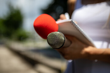 Journalist at news conference, writing notes, holding microphones