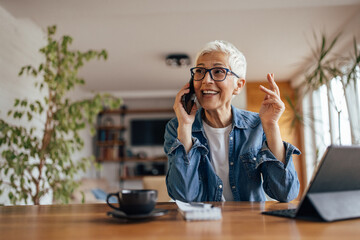 Senior woman, talking over the phone, at her home office.