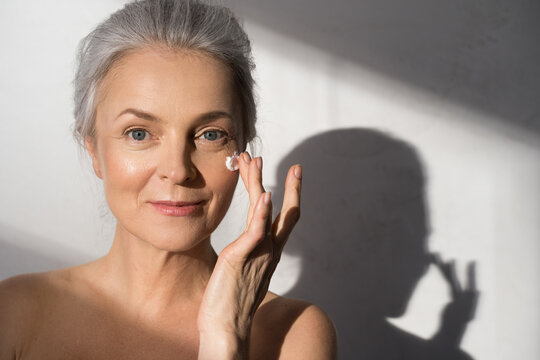 Woman applying cosmetic cream on clean hydrated skin portrait