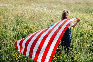 Close up back view of little playful preschool girl run across green field with national USA flag outdoors at summer day. American flag, country, patriotism, independence memorial day july fourth