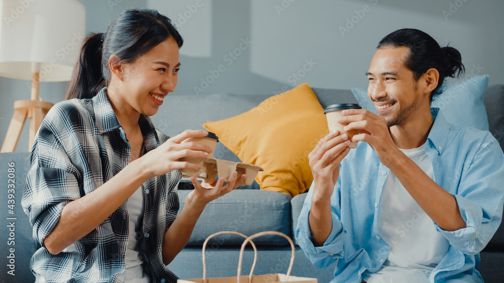 Wall mural happy asian young attractive couple man and woman sit at new home drink coffee relax and talk smile 