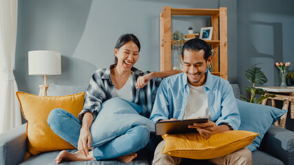 Happy asian young attractive couple man and woman sit on couch use tablet shopping online furniture...