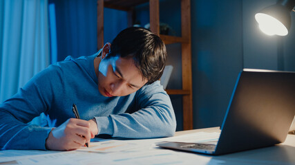 Asian freelance businessman focus work type on laptop computer busy with full of paperwork chart on...