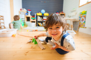 Little boys play with a wooden railroad in a stylish nursery.
