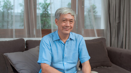 Portrait Asian Chinese senior man feeling happy smiling at home. Older male relax toothy smile looking to camera while lying sofa in living room at home in the morning concept. © tirachard
