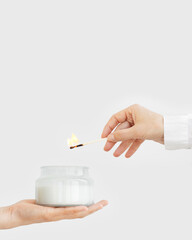 Female hand uses matchstick to light fragrant candle in glass jar with natural ingredients