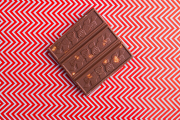 Close-up piece of brown chocolate bar with red and white background.
