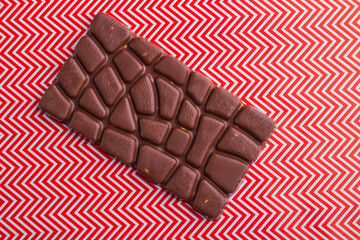 Top view one single chocolate bar on red and white background.