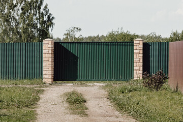 The road to the gate. Green corrugated fence. Sliding gates.