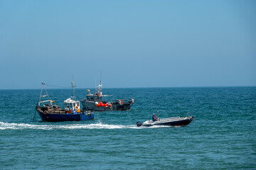 Naklejka premium speed boat passing fishing trawlers in the sea