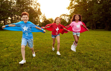 Happy kids in superhero costumes running on meadow