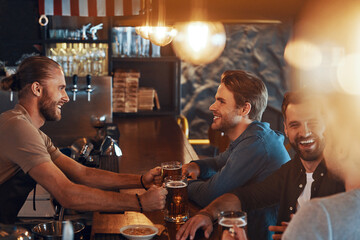 Top view of smiling young men in casual clothing drinking beer and bonding together while sitting in the pub
