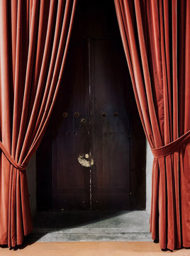 A wooden door hidden behind an open red curtain made of velvet
