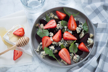 Plate with beetroot, strawberry and gorgonzola cheese salad on a light-grey marble background, horizontal shot