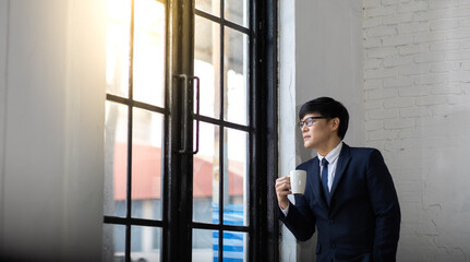 successful asian businessman drink coffee and looking through window in the city. CEO or business owner.