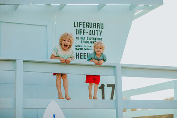 Curly young boys in summer clothes posing at blue lifeguard tower. Summertime.