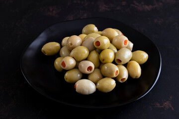 Green olives stuffed with peppers on a dark background. Tasty green olives in the plate.