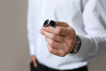 Stylish man holding cufflinks against beige background, closeup