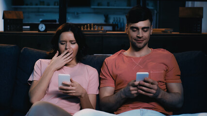pleased man and tired woman using cellphones in modern living room.