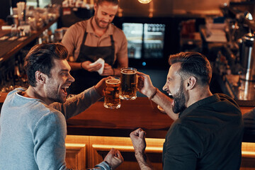 Top view of carefree young men in casual clothing drinking beer while sitting in the pub