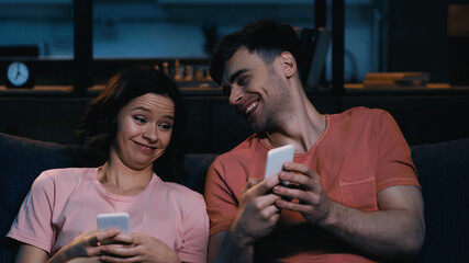 joyful man and woman looking at smartphone and smiling in modern living room.