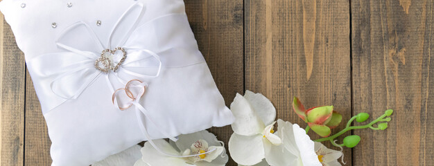 banner with white orchid and pillow for wedding rings with rings with rhinestone hearts on a wooden background.
