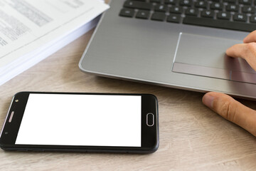 Smartphone with blank screen, laptop and sheets around. Concept of person in the office looking at his smartphone.