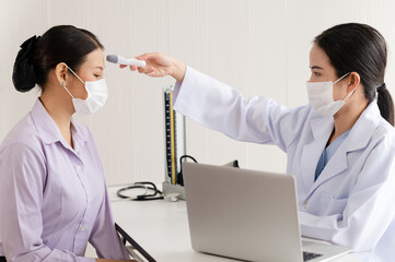 Asia Female doctor checking the temperature of a young woman patient with a digital thermometer at...