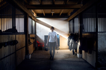 Portrait of a girl preparing her horse for riding.She wears a helmet and holding a whip.