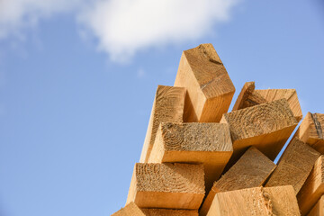 Stacked lumber on blue sky. Folded wood. Closeup wooden boards. The surface of the end of the board.Lots of planks stacked on top of each other in the warehouse. Lumber for use in construction. 