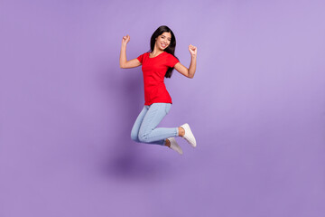 Fototapeta na wymiar Full length photo of pretty lucky young lady wear red outfit smiling jumping high rising fists isolated violet color background