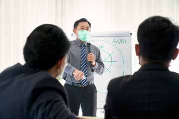 Asian lecturer or manager presenting about sales target point on flip board in seminar room with businessman audience