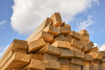 Stacked lumber on blue sky. Folded wood.Closeup wooden boards. The surface of the end of the board. Lots of planks stacked on top of each other in the warehouse. Lumber for use in construction.