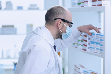 Man pharmacist in protective face mask working in drugstore