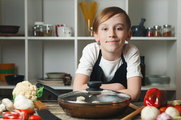 Portrait of cute little chef in kitchen. Boy wearing apron. Kid dreaming of future profession.