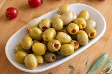 Schilderijen op glas Green olives stuffed with peppers. Tasty organic green olives in the plate. Stuffed olives on wooden background © enezselvi