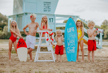 Kids posing on the sand beach with lifeguard tower and surfboard. Happiness.