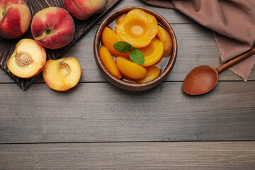 Canned peach halves in bowl on wooden table, flat lay. Space for text