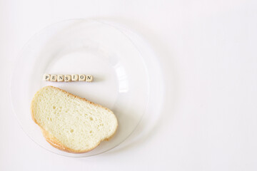 Piece of bread in a transparent plate next to the inscription pension. Minimum pension and old age poverty concept. Blank copy space for inscription