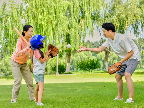 Happy family of three playing baseball in the park