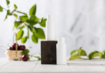 White tubes with cosmetics on a wooden podium against the background of foliage, cherry berries. Natural cosmetics. 