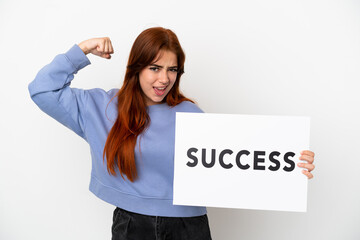 Young redhead woman isolated on white background holding a placard with text SUCCESS and doing strong gesture