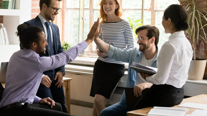 Happy young african american employee giving high five to caucasian colleague, celebrating coming...